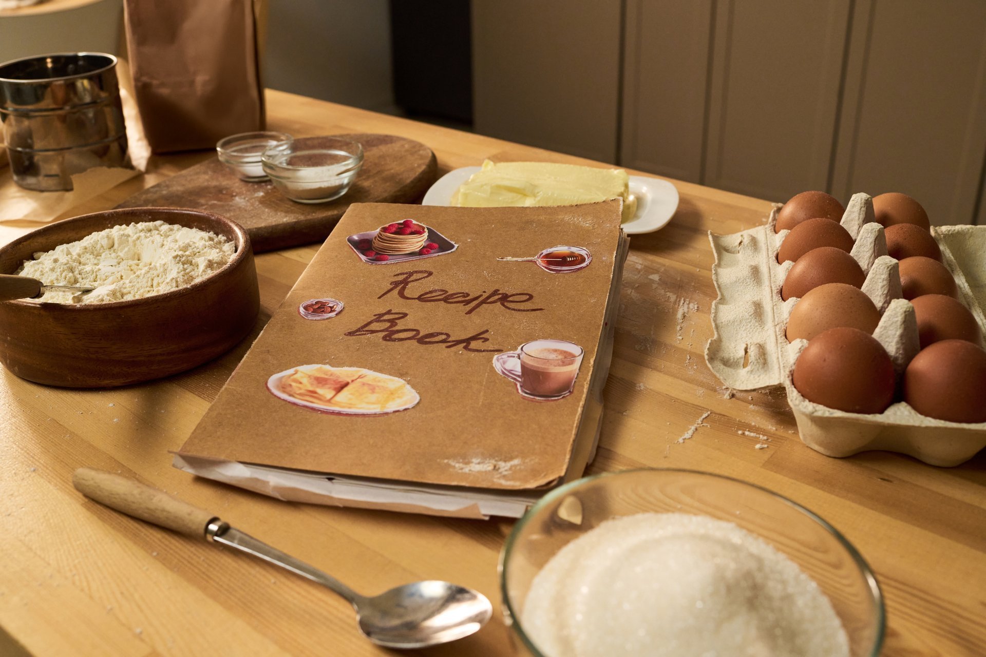 Open cookbook surrounded by fresh baking ingredients, eggs, flour and utensils on a wooden table